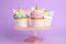 Cute sweet unicorn cupcakes on dessert stand against violet background