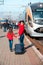 Cute sympathetic beautiful smiling young mother with daughter and suitcase on train background on railway station platform