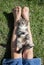 Cute tabby kitten lies on its back on the feet of a barefoot child sitting on the grass