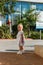 Cute tanned girl in white lace dress and sandals stands on the hotel grounds in the summer