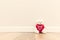 Cute teddy bear with big red plush heart. Sitting on wooden floor against white wall.