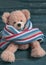 Cute teddy bear with colorful scarf sitting on blue wooden backg