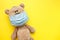 Cute teddy bear with face mask on his mouth on yellow background. Quarantine concept, covid-19 virus protection. Flat lay, top