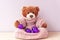 Cute teddy bear in knitted sweater with little lilac Christmas balls. New year greeting postcard