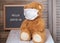 a cute Teddy bear in a medical mask sits at home against the background of a wind Board with the text in English hello covid-19.