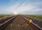 Cute teddy bear sitting on the rails, perspective view. Far away on the horizon, beautiful sky, sunrise and windmill. Travel or