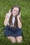 Cute teen girl in headphones enjoys the music on the green grass in park. Love of music.