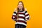 Cute teen girl in a striped casual sweater asks on a yellow background with copy space
