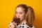 Cute teenage girl with a two-ponytail hairstyle eats chocolate chip cookies on a yellow background