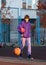 Cute teenager in violet hoodie playing basketball. Young boy with ball learning dribble and shooting on the city court. Hobby