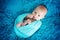 Cute three months old baby boy in blue wrap, lying on a blue blanket, looking curiously