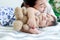 Cute toddle baby girl infant sleeping during hug teddy bear toy on bed, young beautiful mother gentle touch sleepy daughter kid,