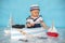 Cute toddler baby boy in wooden boat, playing with fishes, starfish and binoculars as sailman