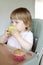 Cute toddler, baby girl in baby chair feeding eating a muffin. Delicious healthy home baked food for kids