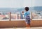 Cute toddler baby watching the cityscape from the rooftop patio with glass balustrade