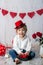 Cute toddler blond child with cute hat, sitting on little sofa with Valentine decoration, isolated background
