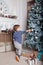 Cute toddler boy decorates Christmas tree in living room near fireplace with New Year decorations, gifts