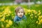 Cute toddler boy having fun between rows of beautiful yellow daffodils blossoming on spring day