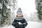 Cute toddler boy having fun on a walk in snow covered pine forest on chilly winter day. Child exploring nature