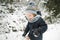 Cute toddler boy having fun on a walk in snow covered pine forest on chilly winter day. Child exploring nature