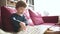 Cute toddler boy reading books on the sofa at home on a bright sunny afternoon