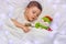 A cute toddler boy is sleeping on white linen with his favorite toy snowman in the blue lights of the garland.