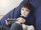 Cute toddler boy wearing school uniform laying down on blue bean bag chair watching tablet with teddy bear at kid room, Kid and te