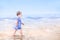 Cute toddler girl in blue dress walking on beach