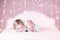 Cute toddler girl and her newborn baby brother on bed under romantic pink lights
