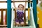 Cute toddler girl playing on slide on outdoor playground. Beautiful baby in colorful shorts trousers having fun on sunny