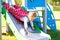 Cute toddler girl playing on slide on outdoor playground. Beautiful baby in red gum trousers having fun on sunny warm