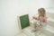 Cute toddler girl in silver head bound writing on chalk blackboard, sitting