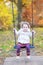 Cute toddler girl on swing with autumn trees