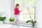 Cute toddler girl watching out window in white kitchen