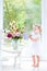 Cute toddler girl in white dress watering flowers