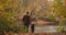 Cute toddler is holding hand of his father in forest, man and child are standing together on calm shore of lake at