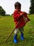 Cute toddler standing on meadow with stick and red farmers jacket