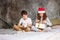 Cute tween children in Santa hats and pajamas open christmas gift boxes on bed with pillow, christmas morning time, kids party