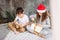 Cute tween children in Santa hats and pajamas open christmas gift boxes on bed with pillow, christmas morning time, kids party