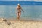 Cute tween girl in hat and bikini getting out of water after swimming in lake Baikal in summer sunny day. Beautiful young lady