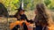 Cute twin girls dressed like witches are fighting and laughing in a forest.