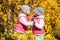 Cute twin sisters, embrace and kissing on a background field with yellow flowers, happy cute and beautiful sisters having fun with