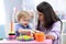 Cute woman with child playing with plastic blocks at home or kindergarten