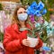 Cute woman gardener in face mask chooses blue phalaenopsis flowers in store. Buying indoor plants for home gardening with