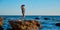 Cute woman posing on sharp cliff. Lady wearing trendy hat. Breathtaking seascape. Beach and relax concept, copy space