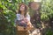 Cute woman viticulturist inspecting vines with ripening grapes while carrying a wooden crate with freshly harvested crop