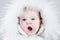 Cute yawning baby girl wearing huge white fur hat