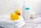 Cute yellow duckling sitting on diapers pile in the white bathroom. Newborn baby equipment. Soap, powder and comb.