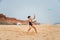 Cute youg girl in swimsuit standing on a beach by the sea throwing a green disc.