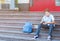 Cute, young boy in blue shirt with backpack holds globe in his hands on the steps in front of his school. Education,